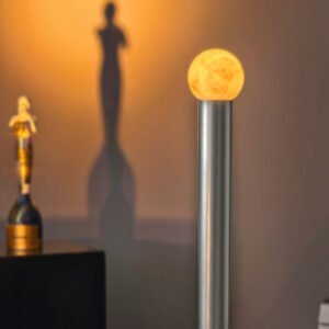 Moon-like glowing orb atop a silver lamp against a warm wall, casting shadows of statues in the background (decorative lamp).