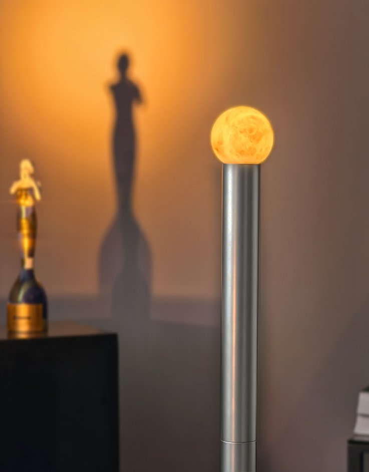 Moon-like glowing orb atop a silver lamp against a warm wall, casting shadows of statues in the background (decorative lamp).