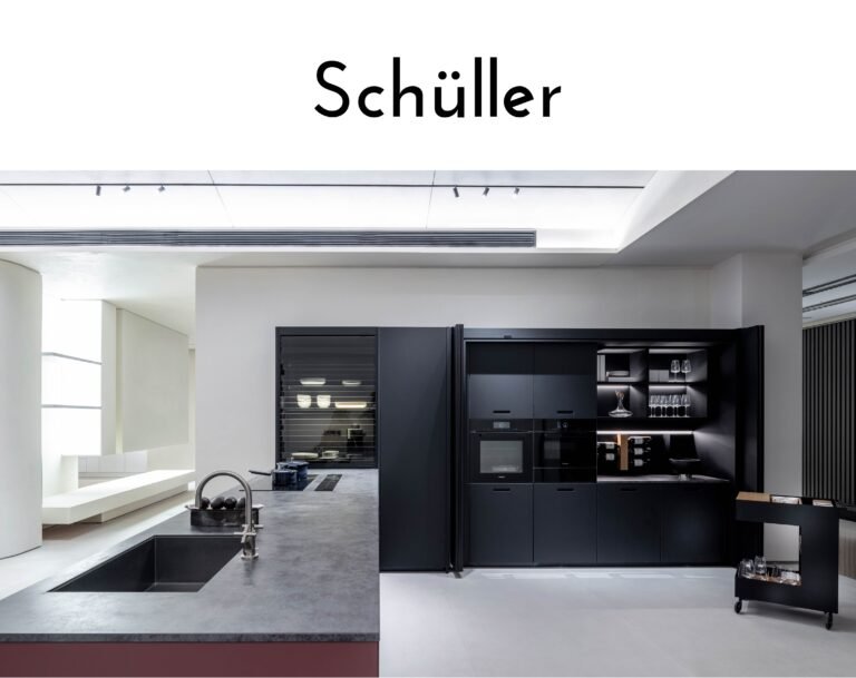 Brand showroom banner reading 'Schüller' above a modern black kitchen display with integrated ovens and glass-front cabinetry